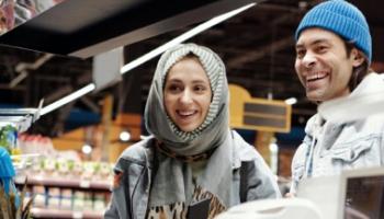 An image of two, smiling customers at the til in a convenience store. 