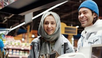 An image of two, smiling customers at the til in a convenience store.