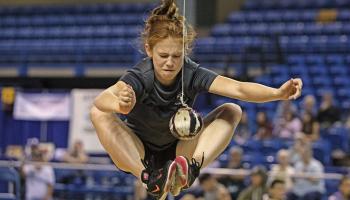 Une femme saute dans les airs pour atteindre avec ses deux pieds joints une balle suspendue au plafond.